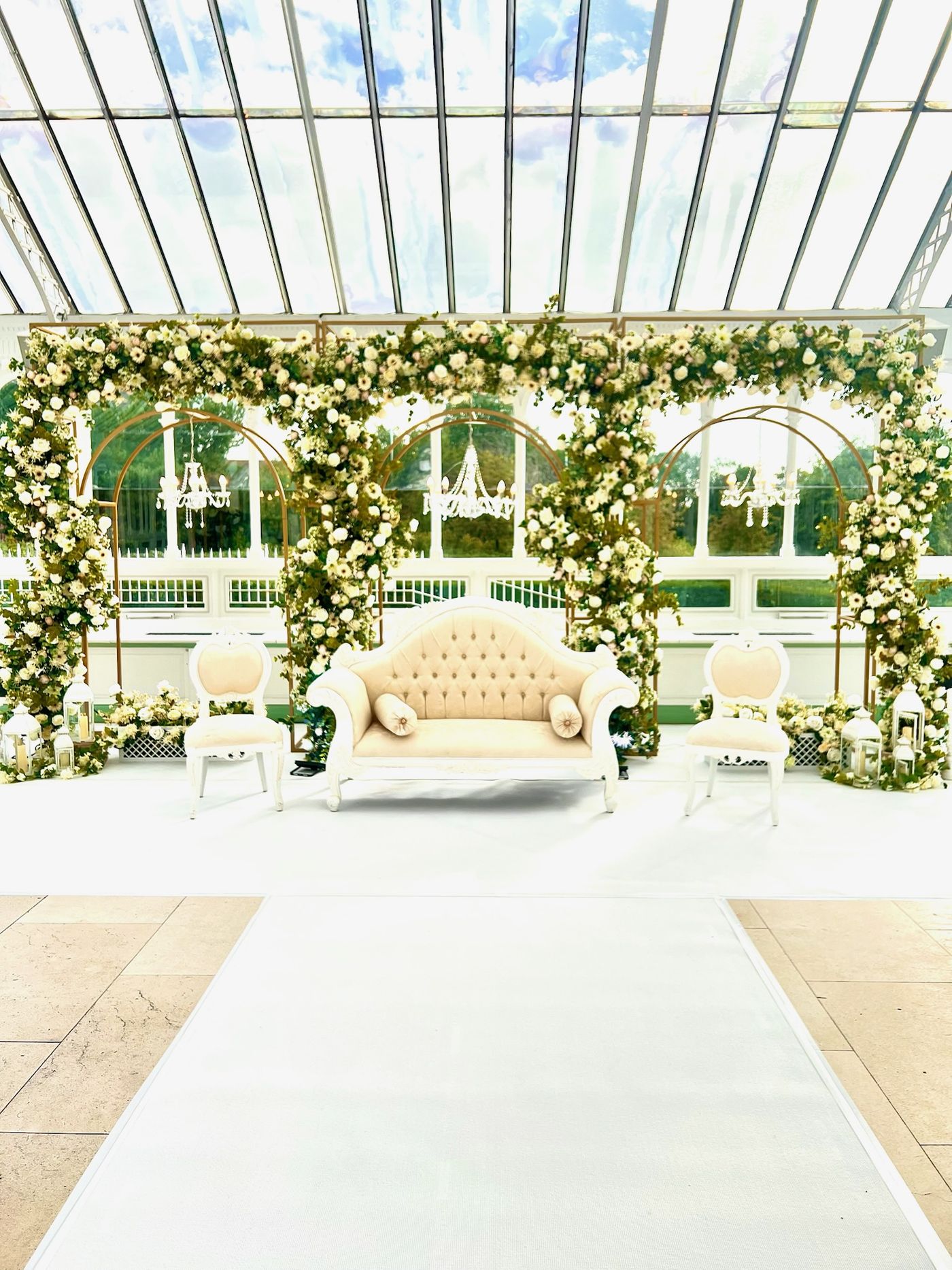 A glass-roofed garden room dressed with floral arches along a walkway