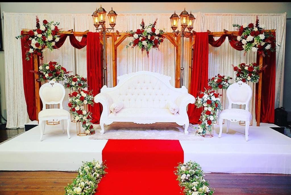 A red and gold stage with an ornate bridal sofa and floral pillars