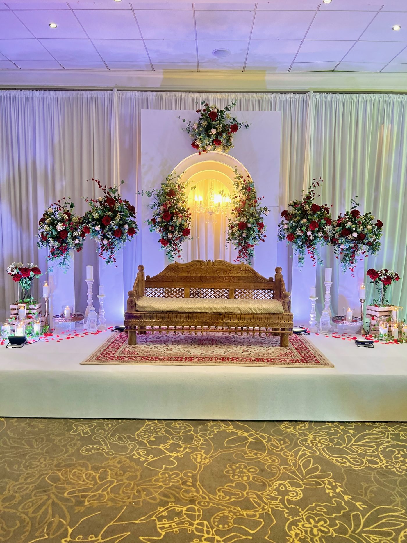 A carved wooden bench dressed with red roses and candles for a Nikah ceremony
