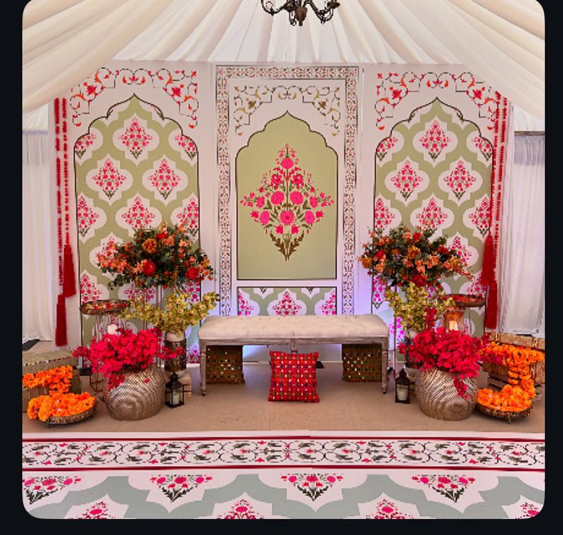An ornate framed panel with orange drapes and floor cushions