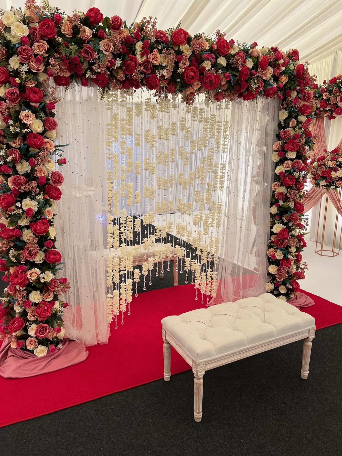 A double floral arch over a red carpet with a cream bench beneath it
