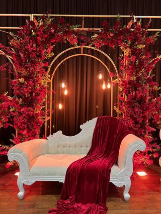 A deep red floral arch with a cream and red chaise