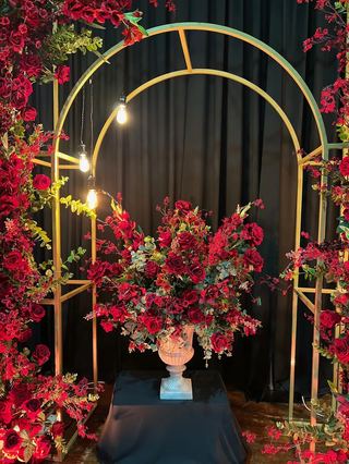 A gold arch dressed in red florals against dark drapes