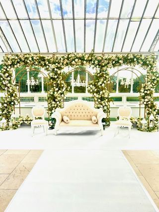 A glass-roofed garden room dressed with floral arches along a walkway
