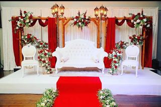 A red and gold stage with an ornate bridal sofa and floral pillars