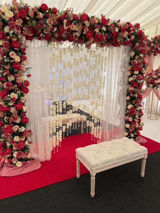 A double floral arch over a red carpet with a cream bench beneath it