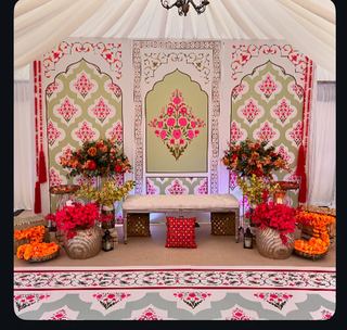 An ornate framed panel with orange drapes and floor cushions