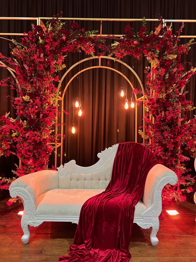 A deep red floral arch with a cream and red chaise