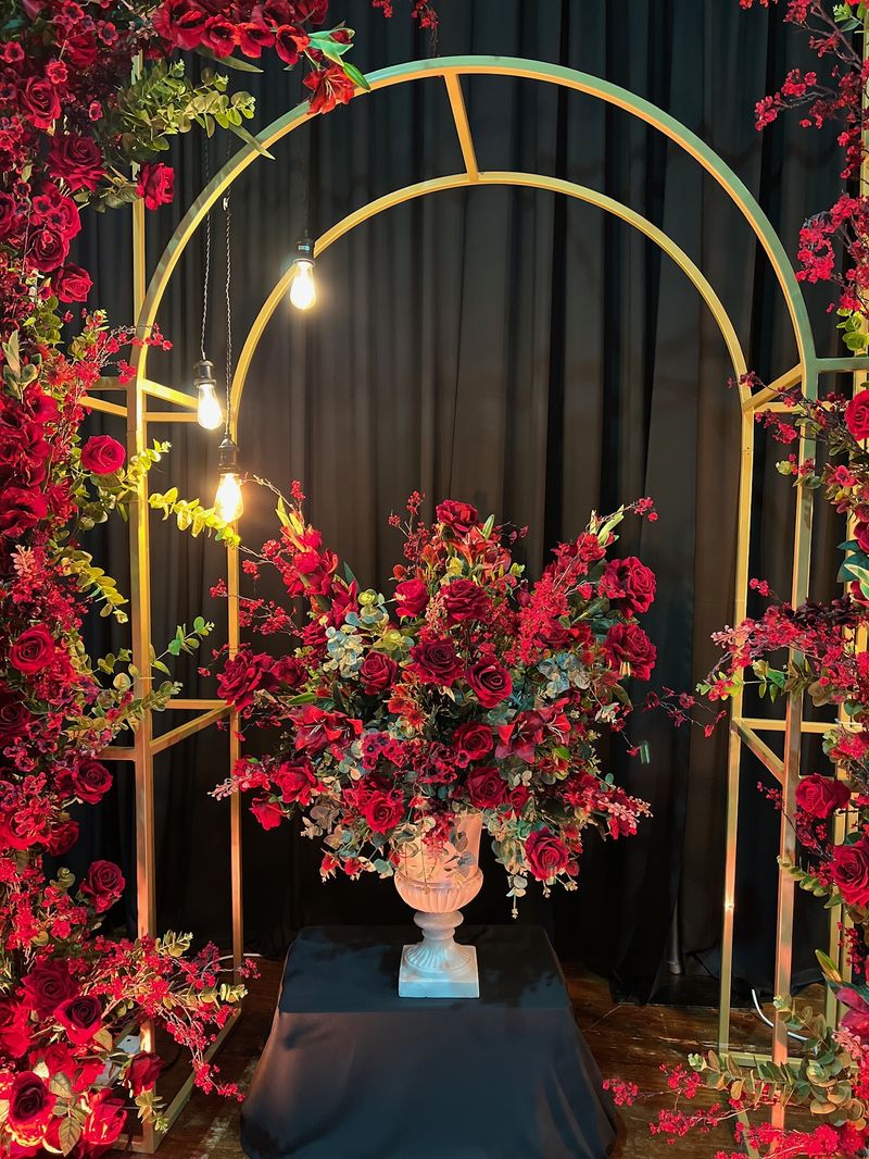 A gold arch dressed in red florals against dark drapes