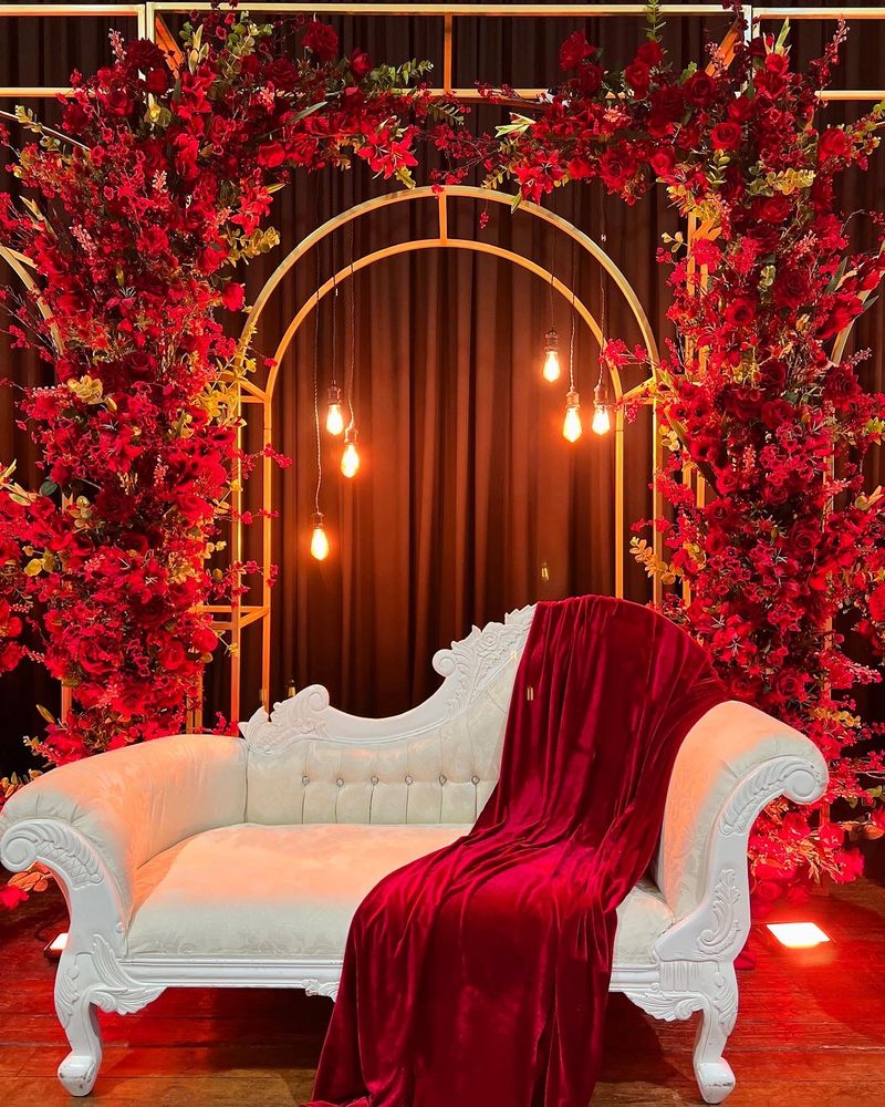 A deep red floral arch above a chaise, with drapes either side