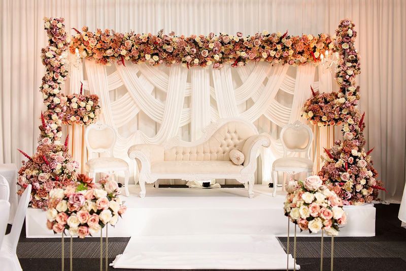 A white and pink floral arch with drapes and a cream sofa