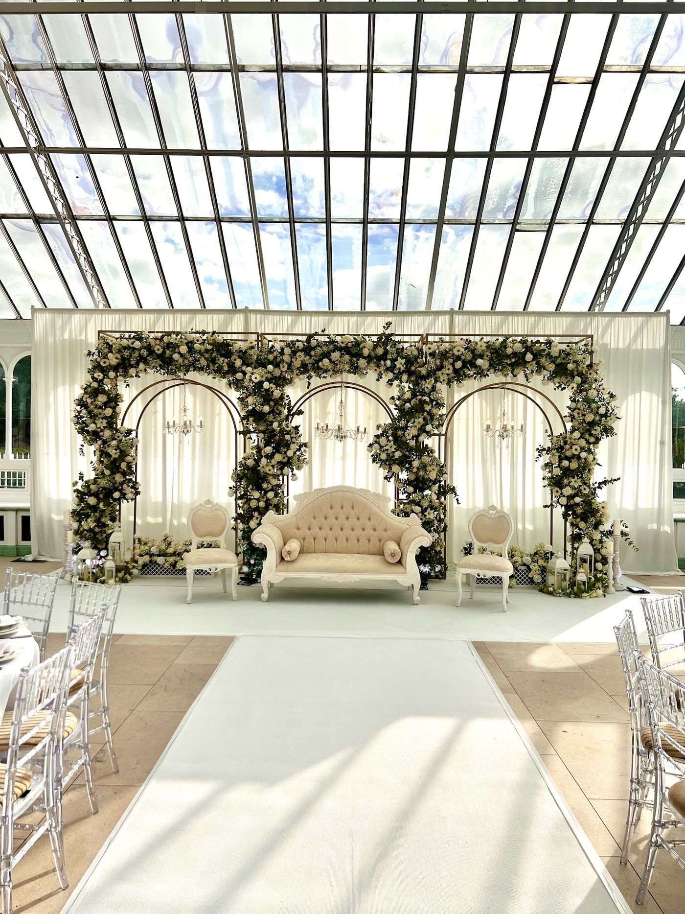 White floral arches over an aisle beneath a glass-roofed atrium